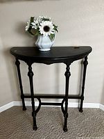 Front view of the semi-circular antique wood table placed against wall with a flower vase on top.