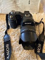 Front view of Sony digital camera with lens hood and Sony branded strap attached.