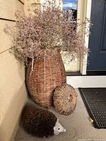 Full view of large wicker basket with lid beside and dried flowers inside, hedgehog boot scraper in front