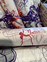 Box contents showing multiple rolled sheets of custom cat-themed wrapping tissue with purple and red cat designs tied with curling ribbon.