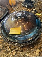 Silver-plated covered casserole dish with ornate twisted handle and lid. The surface shows slight wear and scratches.