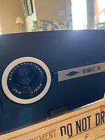 Close-up of slide projector lens showing 'Coated Anastigmat 1.35 Inch' and 'Rotomatic 700' branding on the front panel