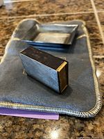Silver rectangular matchbox holder and tray displayed on protective anti-varnish bag.