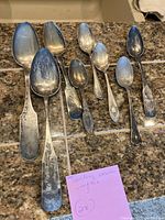 Eight various sterling silver spoons laid on counter with handwritten note describing them.