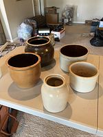 All five stoneware crocks arranged on a folding table showing variety in size and color