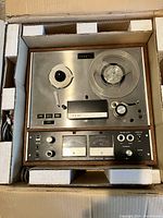 Top view of TEAC reel to reel tape recorder set inside original protective packaging showing metal front panel, wood side panels, reels, and front control panel with buttons and rotary controls.