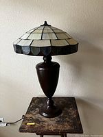 Tiffany style stained glass lamp on top of wooden plant stand table against a wall.