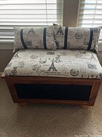 Front view of the cedar chest showing the upholstered top with Paris-print fabric and two matching pillows.