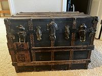 Front view showing metal reinforcements, rivets, lock, and wooden repair patch on trunk