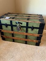 Front view of the large green vintage travel trunk with wood reinforcement slats and black metal hardware including handles and central lock.