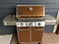 Front view of grill with closed brown enamel lid, stainless steel panel, two-door cabinet and side shelves.