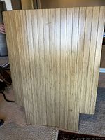 Close-up photo showing two wooden slat floor mats standing upright, natural wood finish with vertical grain.