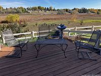 View of loveseat and two rocking chairs around coffee table on outdoor deck with scenic background.