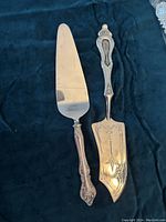 Silver-plated cake servers laid on dark fabric background, showing blade and handle detail for each server