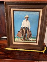 Framed full view of the original cowboy painting showing the entire artwork and frame with tape measure for scale.
