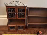 Wooden display cabinet with metal and glass doors, two drawers, beside wooden wall shelves on hardwood floor