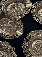 Five ashtrays arranged to show openwork rims and central embossed scenes