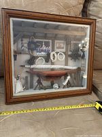 Full view of the shadow box placed on a couch with measuring tape showing size and context