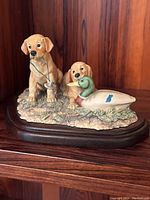 Front view of porcelain sculpture showing two golden retriever puppies with one holding a duck in mouth, mounted on wooden base