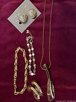 Full view of all jewelry items laid out on purple cloth including bracelets, necklace, pierced and clip-on earrings.