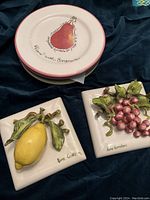 Two porcelain 3D art tiles by Eva Gordon, one with a lemon and one with grapes.