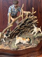 Close-up detail showing man fixing wooden fence with two spaniels nearby, wood base visible beneath, highlighting minor damage on one fence branch.