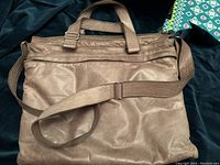 Full front view of the taupe colored lambskin leather padded computer bag with adjustable shoulder strap and handles on dark background.