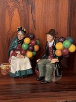 Overall view of the pair of balloon seller figurines, showing the man and woman each holding vibrant balloons.
