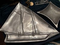 Close up of large shiny pewter sailboat platter with visible rigging lines.