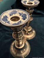 Close-up angled photo showing two silver on copper candle holders with blue floral Delft ceramic wax catchers on top, highlighting the floral detail and metal finish.