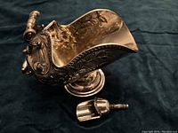 Angled shot of silver plated sugar bowl with floral engravings and small matching scoop placed beside it on dark cloth.