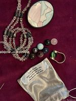 Photo showing the necklace, brooch, ring with changeable stones and storage pouch for stones laid out on a red textured fabric.