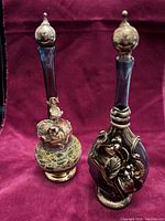 Photo showing two hand blown glass perfume bottles with sterling silver accents placed against burgundy fabric.
