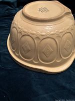 Underside of ceramic bowl showing the rectangular grip handle and embossed circular and diamond pattern on the side.