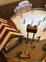 Close-up photo showing detailed miniature figurines at an ice skating rink scene with a ticket booth and part of the ice surface with skaters.
