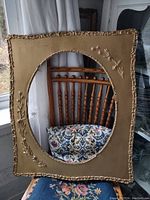 Full view of antique gold wooden frame with oval opening on patterned chair background.