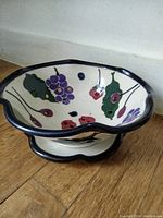 Full view of berry strainer and matching saucer on wooden floor, showing scalloped rims and shape of both.