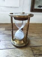 Front view of brass hourglass standing upright on wooden floor.