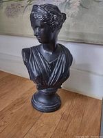 Front and side view of black bust sculpture on wooden surface with classical hairstyle and draped clothing