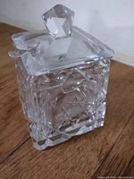 Square glass or crystal mustard pot with intricate cut geometric patterns, shown with the lid on and topped with a faceted knob
