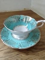 Turquoise and gold Royal Stafford teacup and matching saucer on wooden surface, showing detailed pattern and shape.
