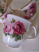 Close-up image of the four Royal Albert mugs displaying pink rose floral designs and gold rim detail on white bone china.