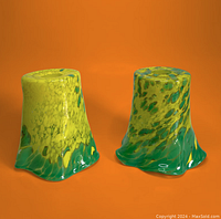 Side view of two colorful glass pendant lamp shades with neon yellow and green colors showing their irregular wavy bottom edges and mottled pattern.