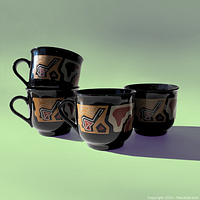 Four black ceramic mugs stacked and arranged, showing abstract geometric pattern in browns, reds, and beige.