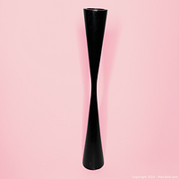 Tall slender black wooden candle holder with a sleek hourglass shape against pink background.