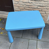 Photo of a blue kids table by IKEA outside on a stone tile floor, showing the tabletop and legs with signs of wear