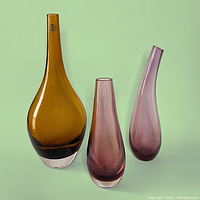Photo showing three glass vases on a green background: tall amber vase (13"), tall purple vase with bent neck (9.5"), short purple cylindrical vase (8") arranged left to right.