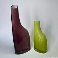 Two glass vases against a plain background, one tall purple and one shorter green