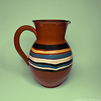 Front side view of ceramic pitcher showing shape, handle, and multicolored horizontal glaze bands.