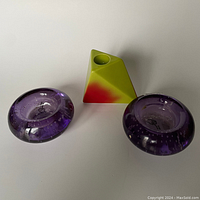 Photo showing two purple IKEA glass tea light holders and one colorful geometric candlestick holder on a neutral surface.